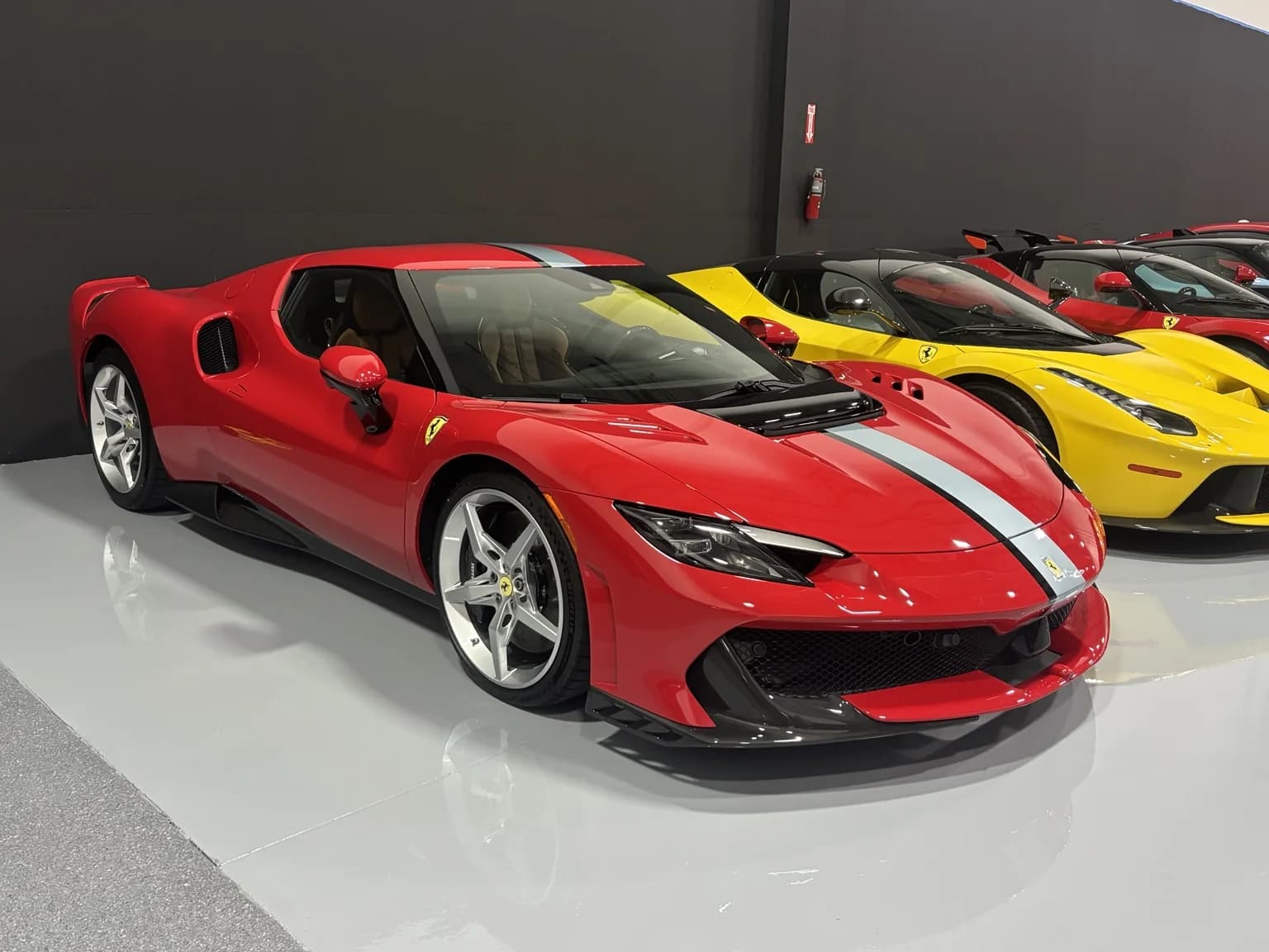 Red Ferrari 296 with a silver racing stripe beside a yellow LaFerrari
