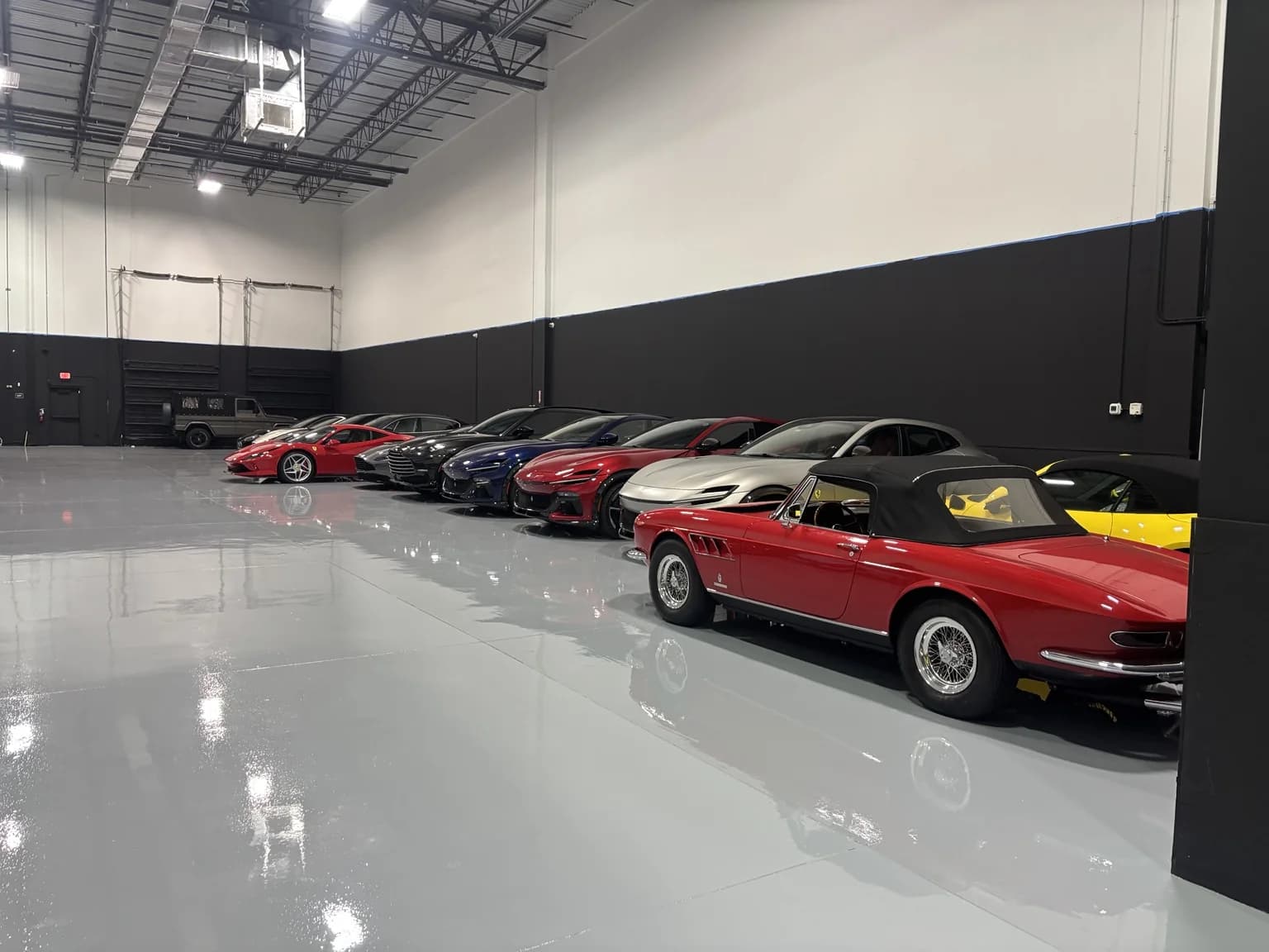 A classic red Ferrari convertible leading a row of modern Ferraris and Aston Martins